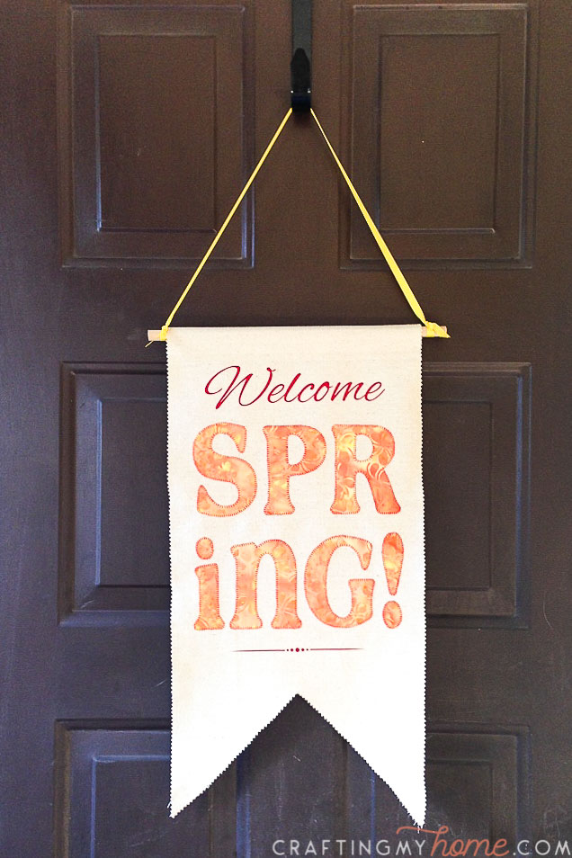 Spring door pennant with design in reds, oranges, and yellows on it hanging on a brown front door. 