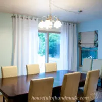Dining room with blue painted walls and white thin curtains with grommets around a sliding glass door.