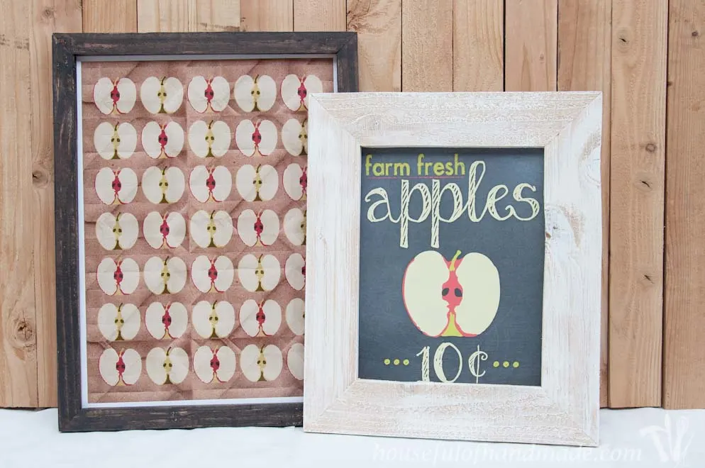All over apple print art in a black frame and farm fresh apples sign in a white picture frame layered together. 