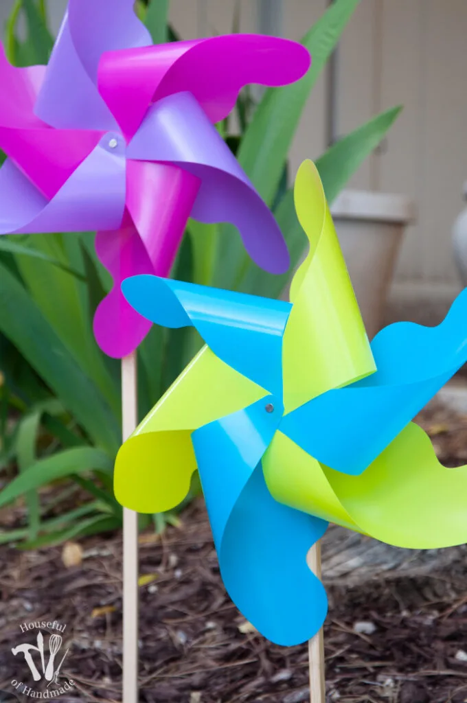 close up of finished pinwheels in garden. set of two pinwheels one in yellow and blue and one in pink and purple
