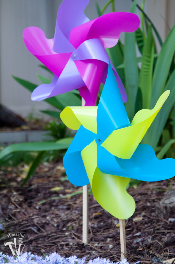 set of two pinwheels in the garden in front of planter and green plant.