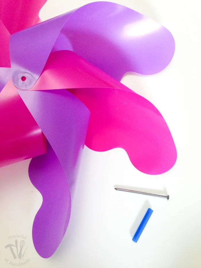 in process photo of pinwheel being put together with nail and dowel in pink and purple