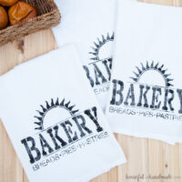 Three tea towels painted with a stencil to say Bakery with a sun burst above it.