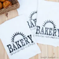 Three tea towels painted with a stencil to say Bakery with a sun burst above it.
