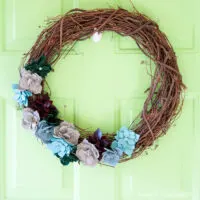 Grapevine wreath with succulents made out of colored leathers on it hanging on a green door.