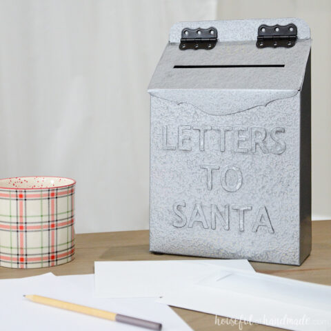 Silver DIY letters to Santa mailbox with black hinges sitting on a table with letters around it.