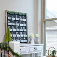 DIY refillable rustic advent calendar on a board up against the wall sitting on a white console table.