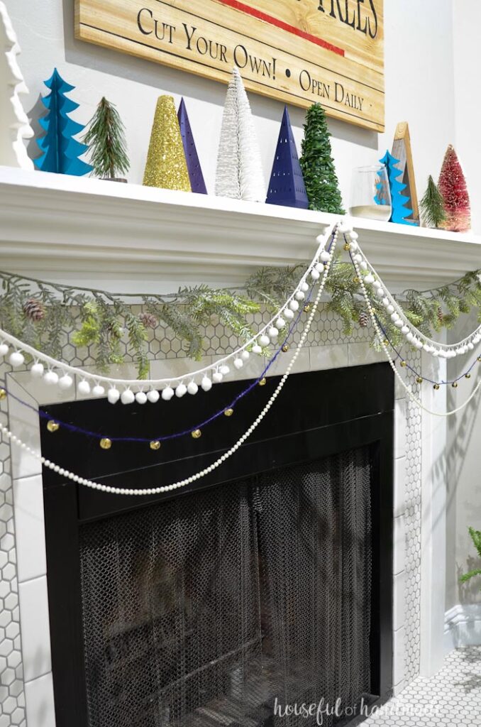Faux pine garland and three strands of decorative trim garland hanging on a fireplace mantel.