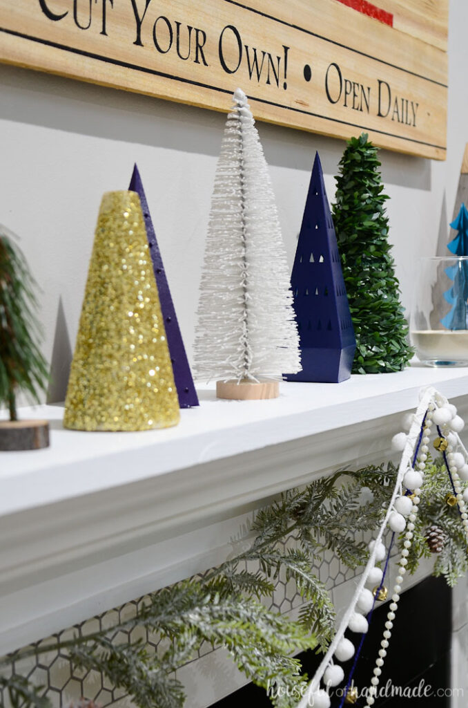 Gold glitter Christmas tree, bottle brush tree, and paper Christmas trees on a white mantel.