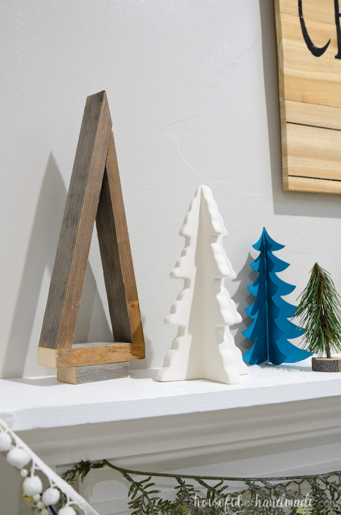 Reclaimed wood decorative Christmas tree and ceramic tree on the edge of a holiday mantel.