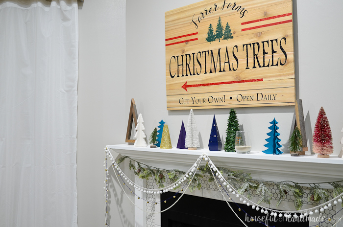 DIY Christmas tree farm sign hanging above a Christmas mantel full of table top Christmas trees.