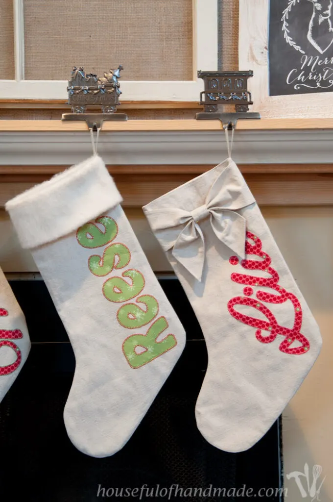 Personalized Christmas stockings made from drop cloth with either fur or a bow on top hanging on a mantel. 