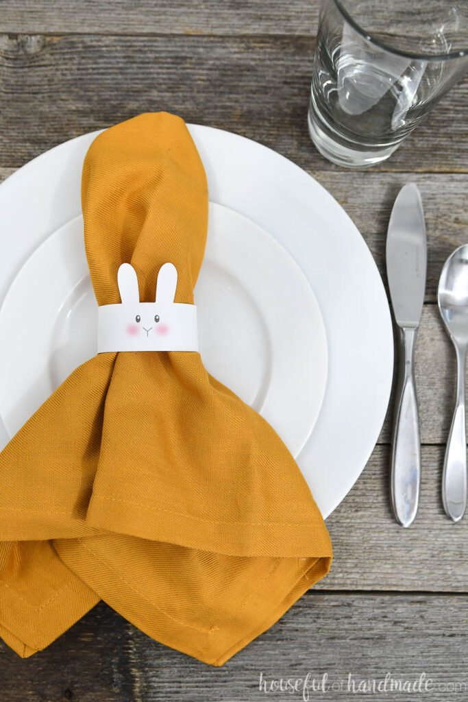 Table set with white plates and a paper bunny napkin ring on a napkin laying on top. 