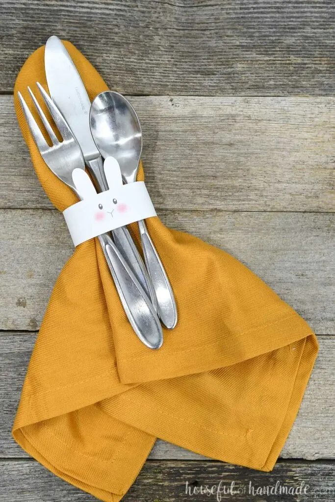 Yellow cloth napkin with bunny napkin ring around it and utensils tucked under the napkin ring.