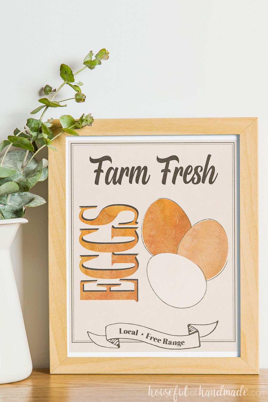 Farm Fresh Eggs printable art in a frame next to a vase of greens. 