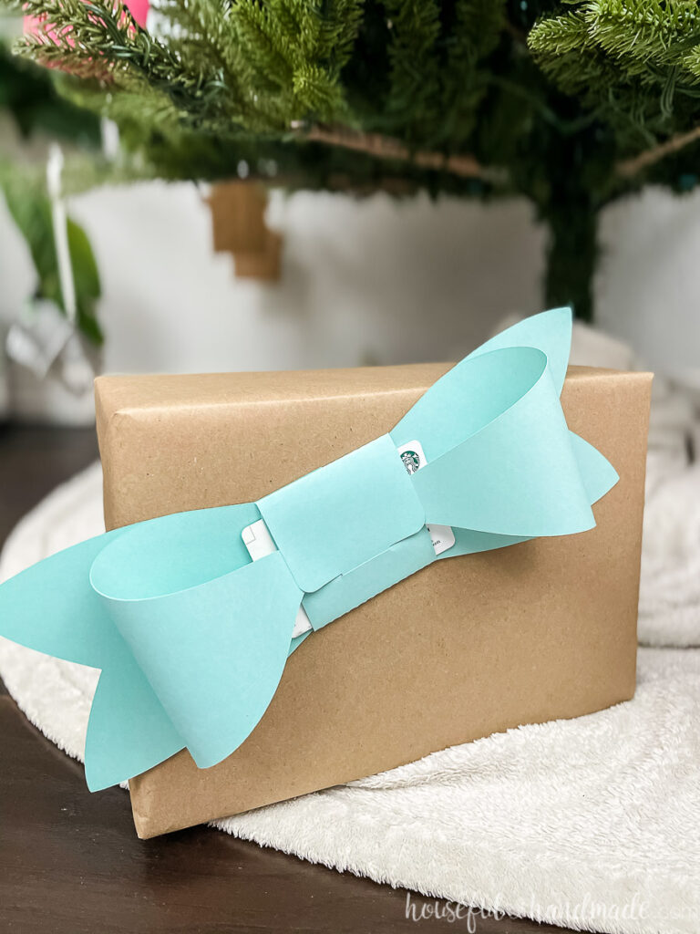 Blue bow shaped gift card holder taped to the front of a present wrapped in brown paper.