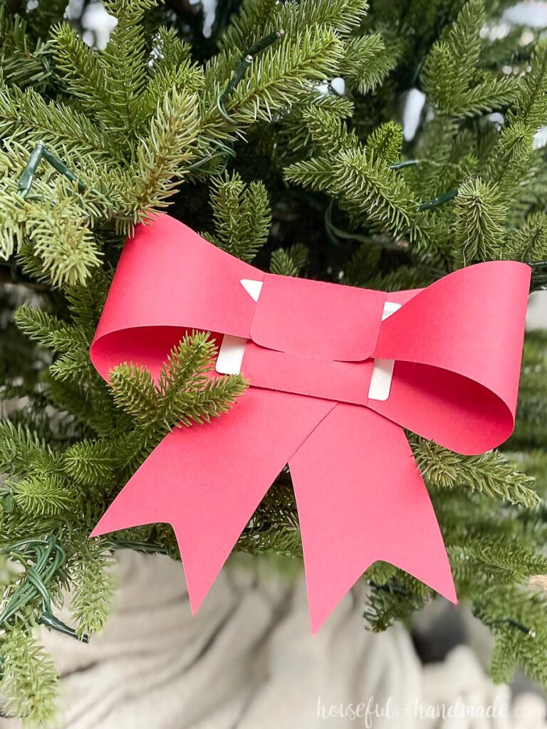 Paper bow gift card holder made from red cardstock tucked into the branches of a Christmas tree.