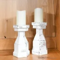 Two faux wood candlesticks with white candles on them.