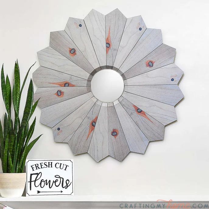 Square photo of the aged wood sunburst mirror hanging next to a plant and fresh cut flowers plaque.