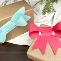 Two gifts under the Christmas tree with bow shaped gift card holders on top.
