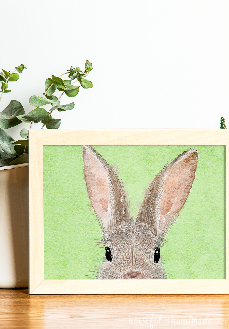 Printable bunny art in a frame in front of a vase of eucalyptus.