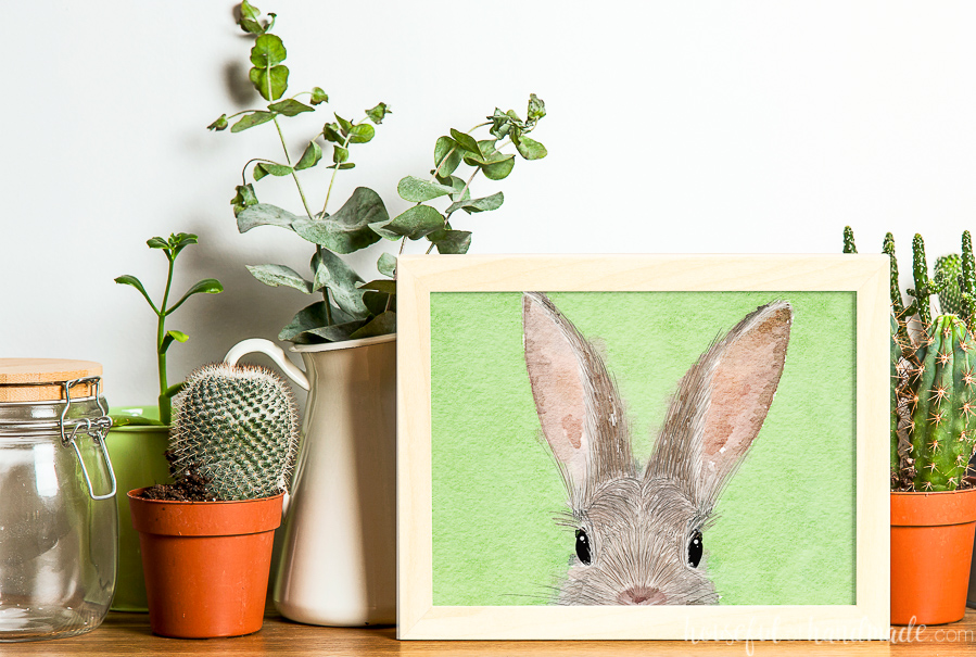 Line of potted plants with a picture of bunny art in a frame.