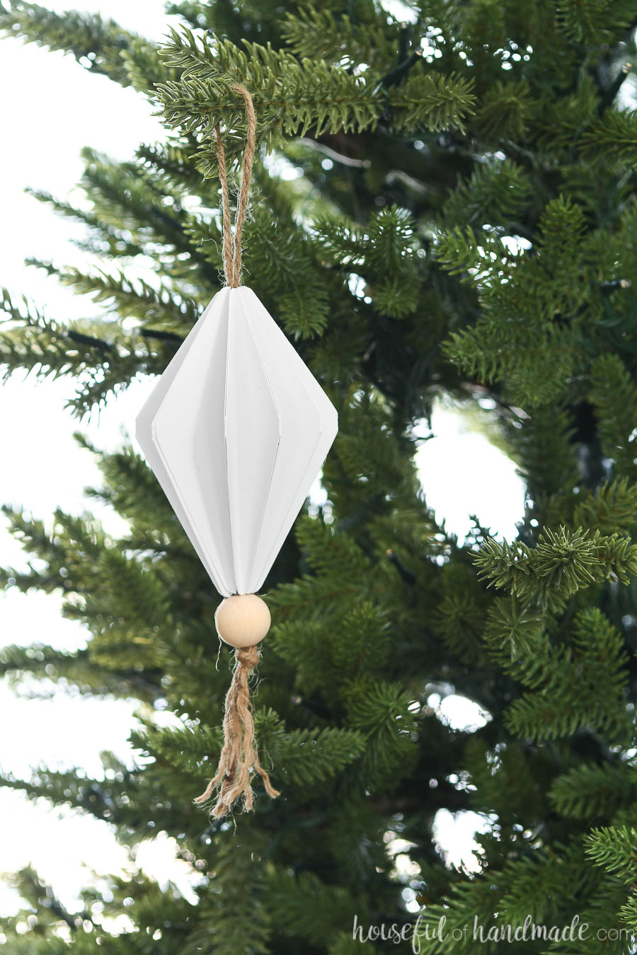 Diamond shaped paper Christmas ornament hanging on a Christmas tree.