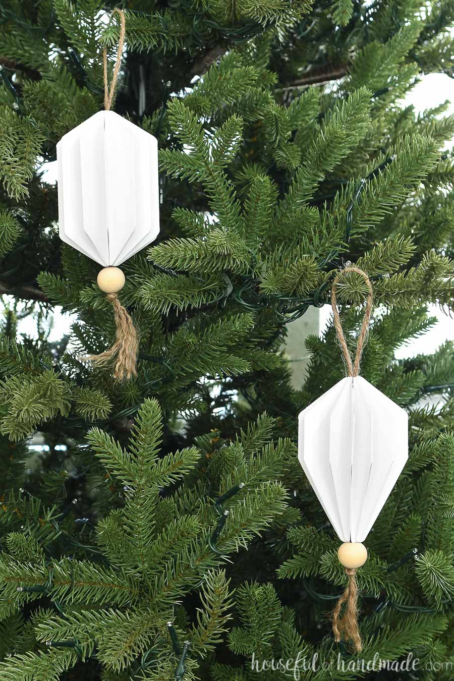 Two jewel shaped Christmas ornaments made from paper hanging on a Christmas tree.