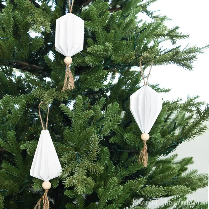 Three white paper Christmas ornaments in the shape of jewels with wood beads and tassels on the bottom.