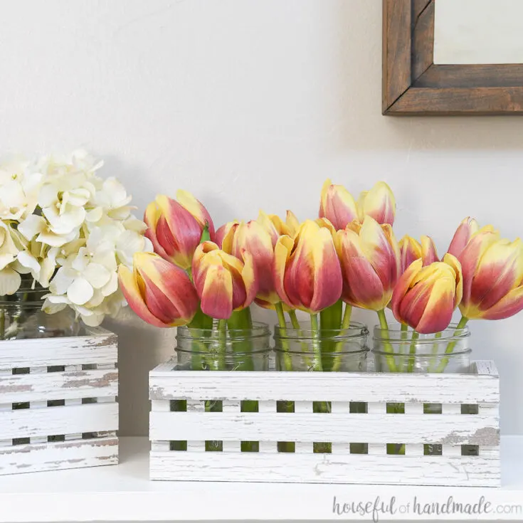 White chippy paint textured trough made from paper holding mason jars full of flowers.
