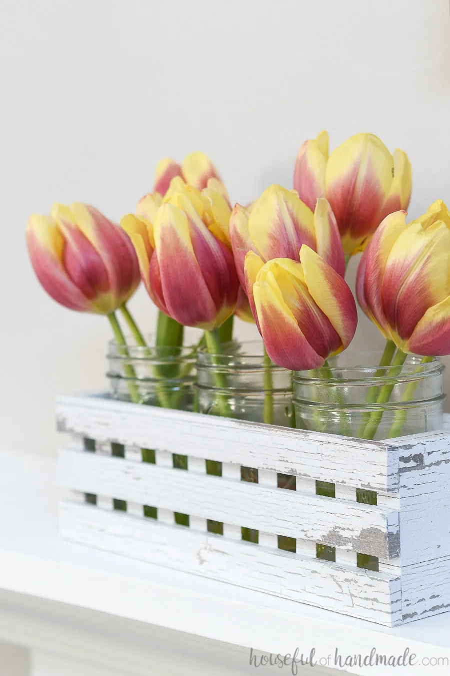 Close up of the tulip blooms in mason jars in a white decorative trough made from paper.
