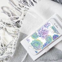 White iphone with the free digital wallpaper for January made of watercolor succulents on the screen.