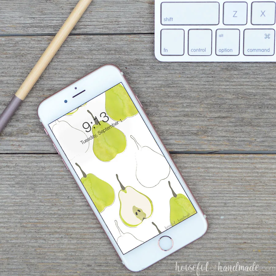 White smartphone with watercolor pear digital background on the screen sitting on a reclaimed wood desk top. 