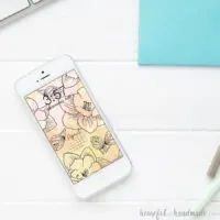 Smartphone sitting on a white desk with free digital wallpaper on the screen.