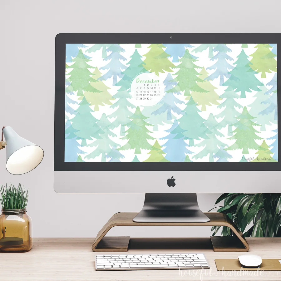 iMac computer on a desk with the watercolor Christmas tree digital background on the screen with the December calendar. 