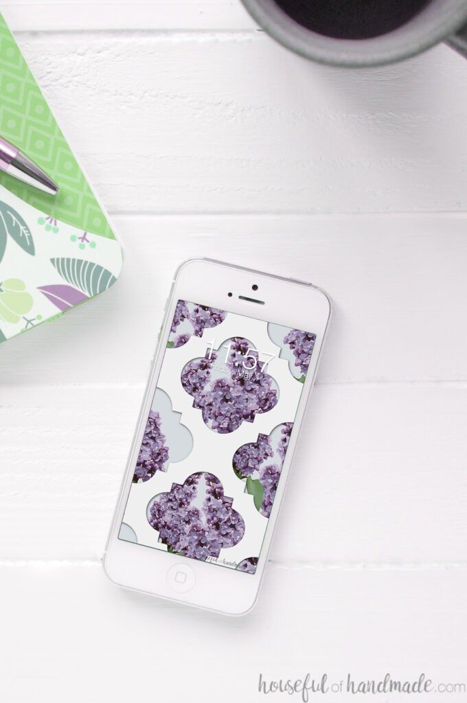 Lilac design digital wallpaper on the background of a white iPhone sitting on a table.