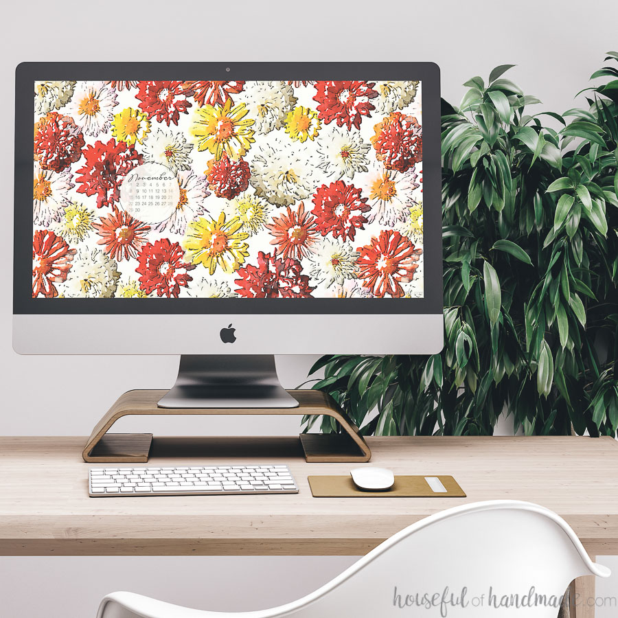 Desktop computer showing the free digital background for November on the screen sitting on a desk in front of a plant. m