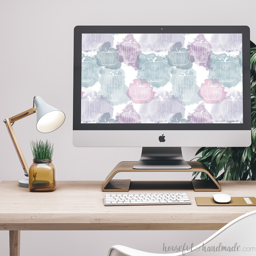 Computer showing the purple & teal pumpkin design wallpaper on a desk with a lamp and plant.