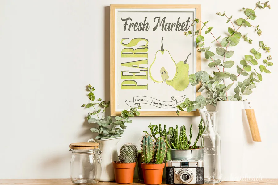 Console table decorated with planted cactus, vases with eucalyptus and a pear fall printable in a frame on the wall. 