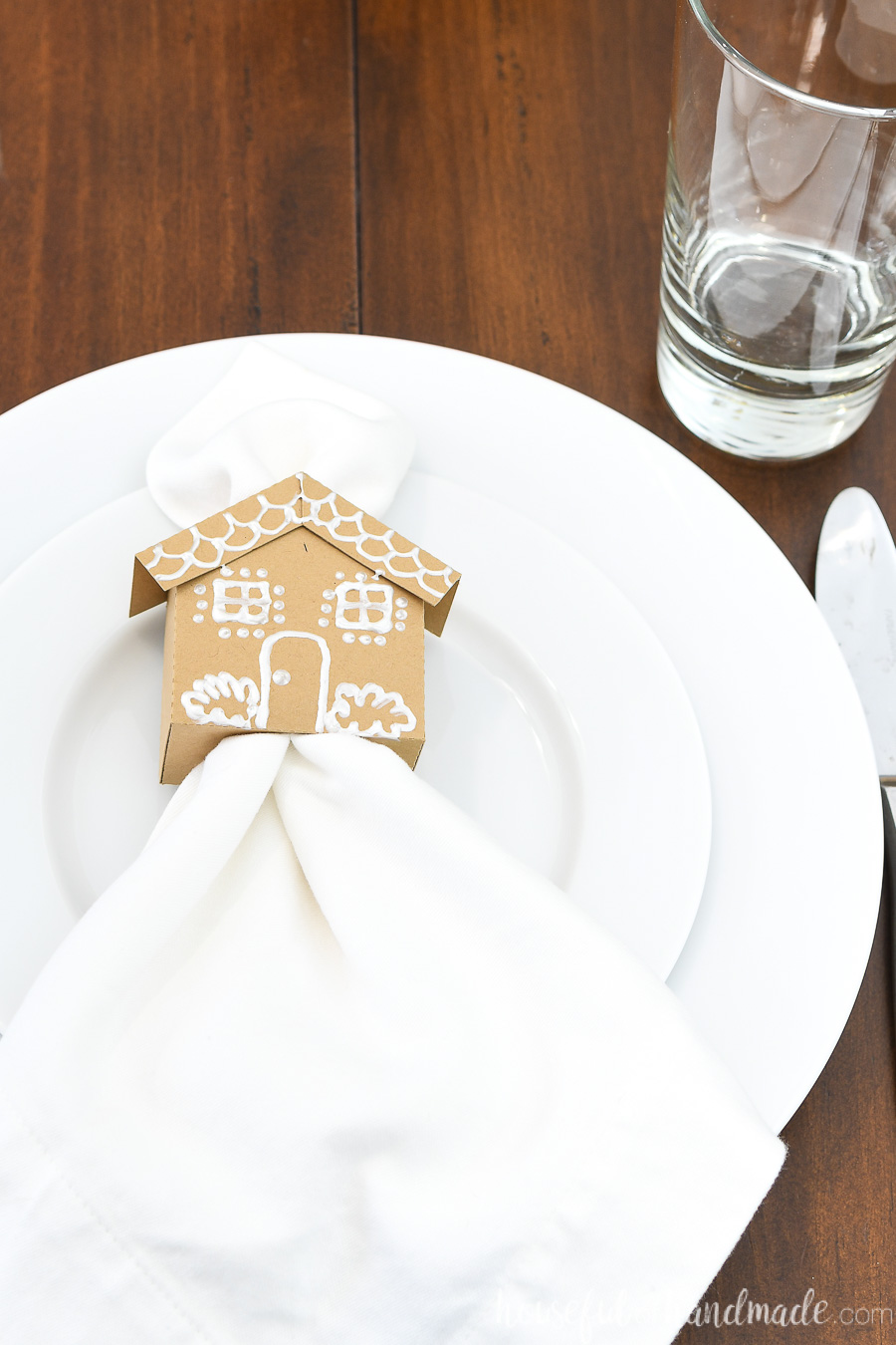 Close up of the paper gingerbread house napkin ring with a white fabric napkin inside sitting on a place setting.