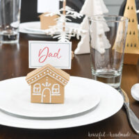 Place setting with a paper gingerbread house place card sitting on top of the salad plate.