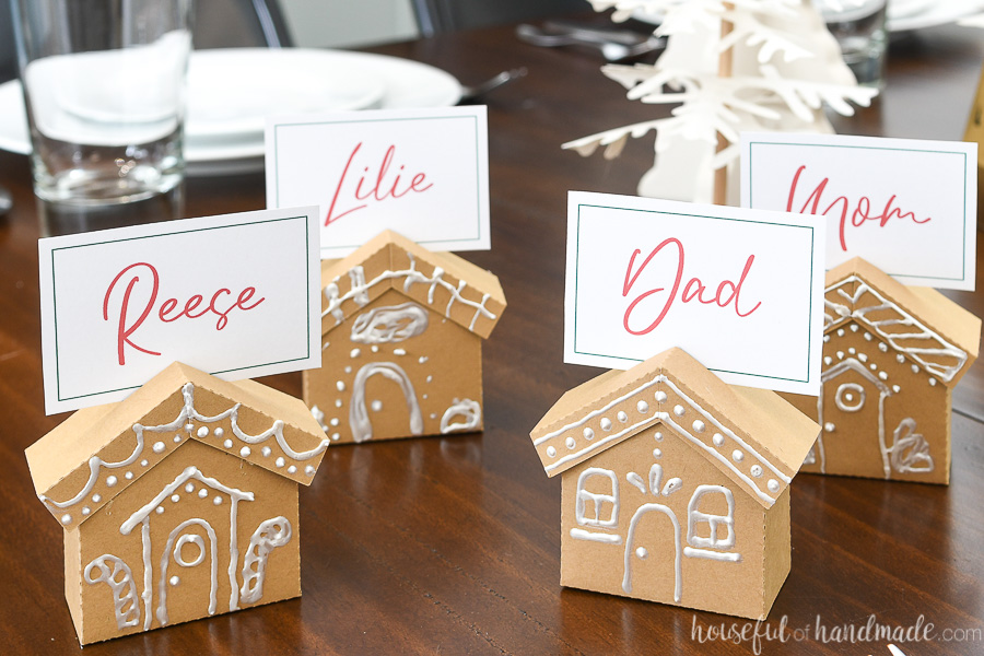 Four gingerbread place card holders made from paper on a table with family names on the place cards. 