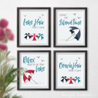 Four lake and beach art prints with beach umbrellas and text on a wall.