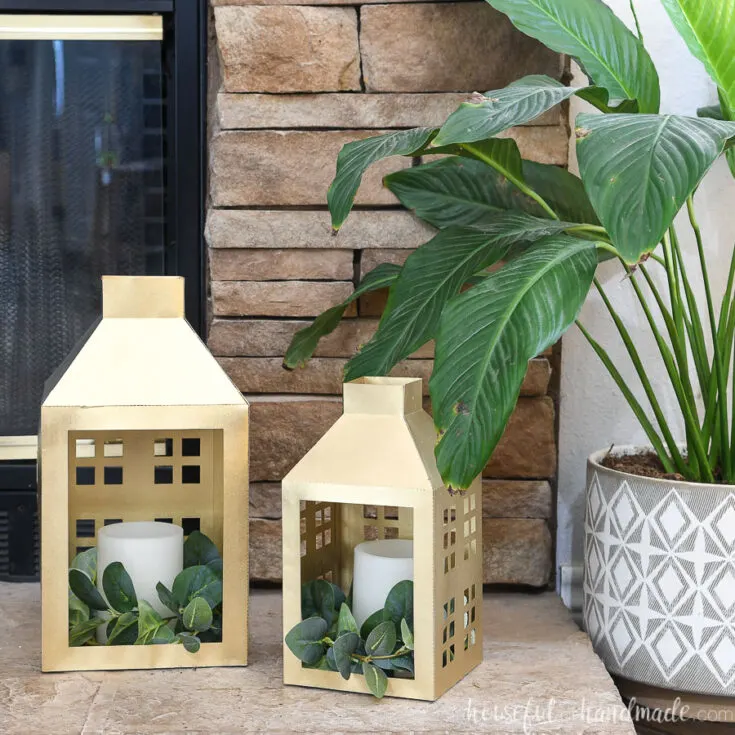 DIY Christmas lanterns painted gold and sitting by the fireplace and a house plant.