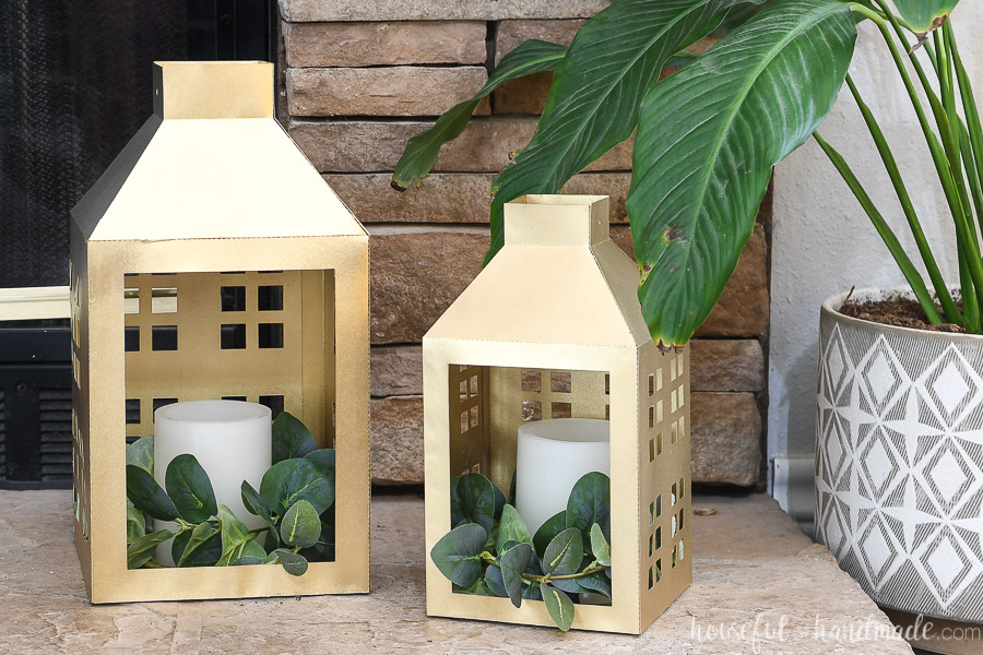 Gold paper lanterns decorated for Christmas on a stone hearth next to a houseplant.