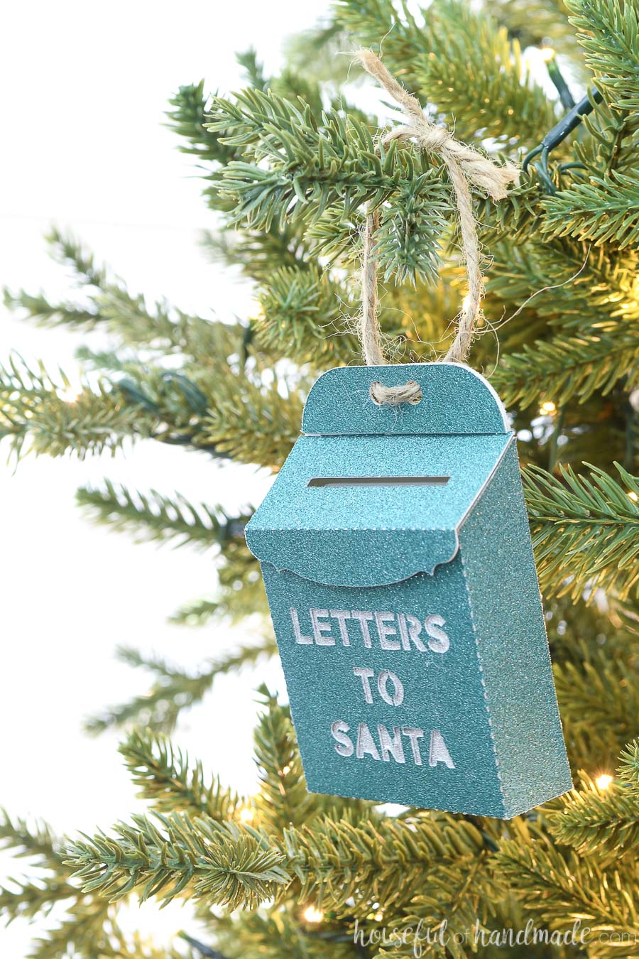 Angled view of the turquoise santa mailbox Christmas ornament hanging on a tree.