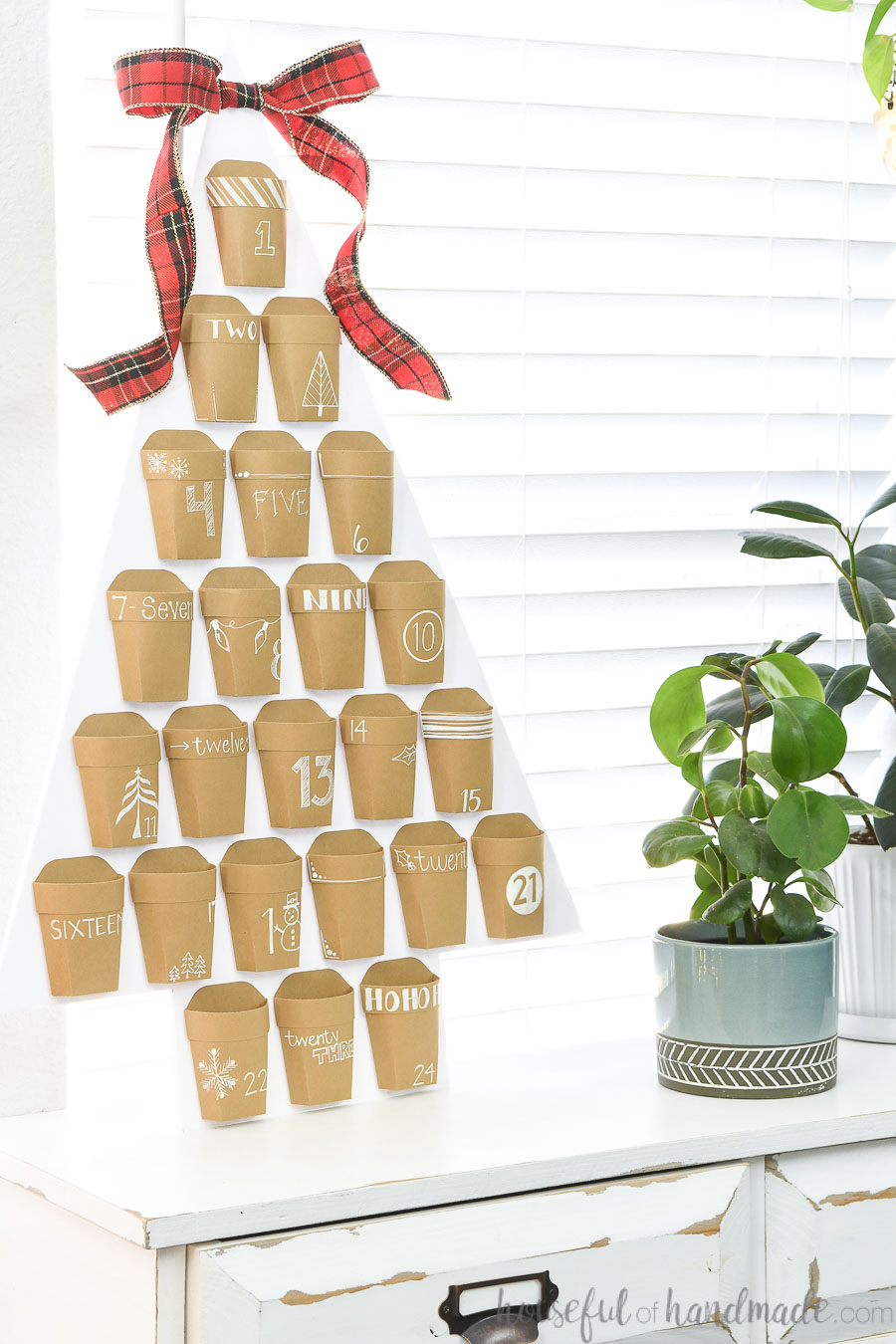 Christmas advent calendar of Kraft paper pockets with white decorations and numbers on a white Christmas tree.