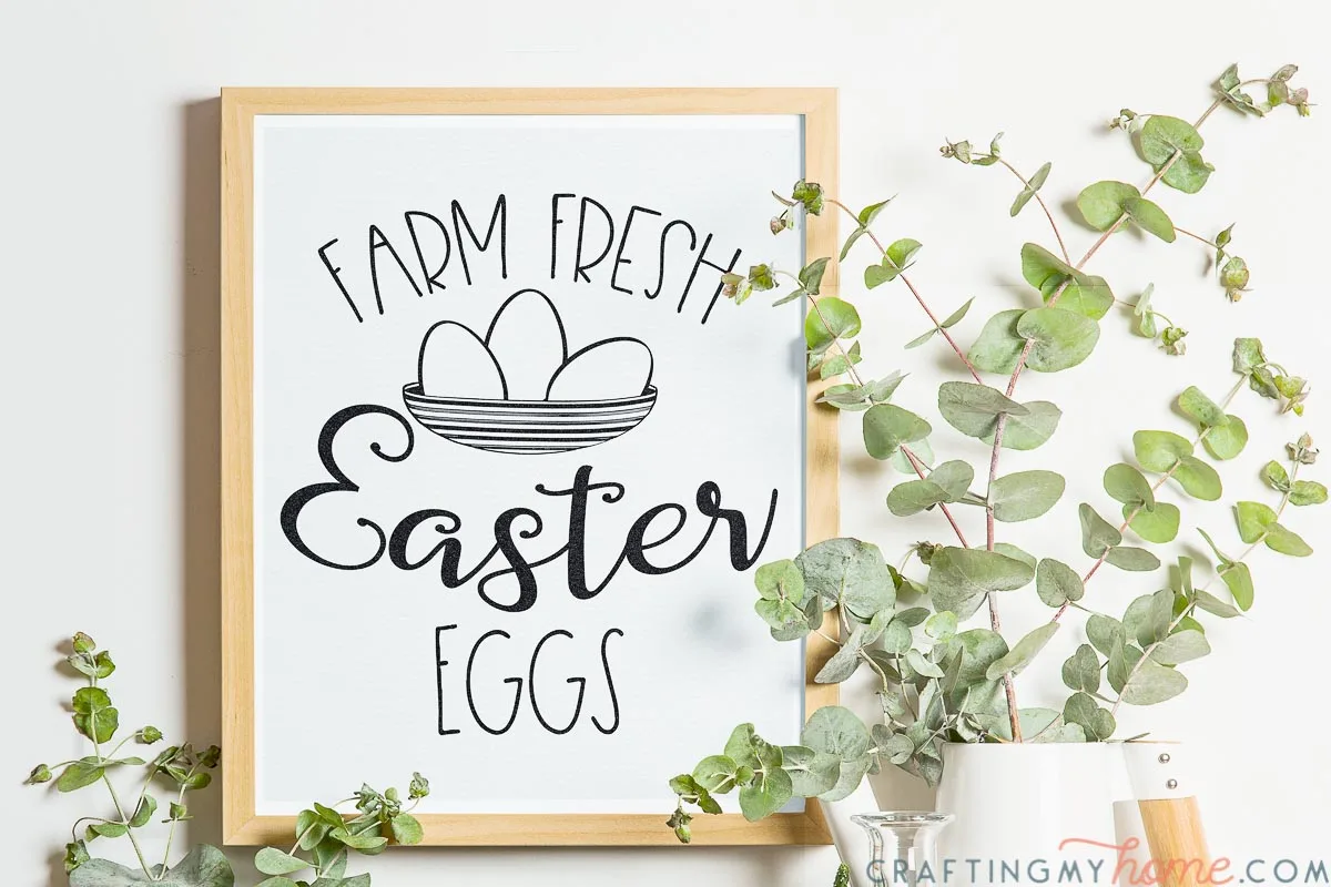 Natural framed photo of the printable Easter sign hanging on the wall with greenery around it. 