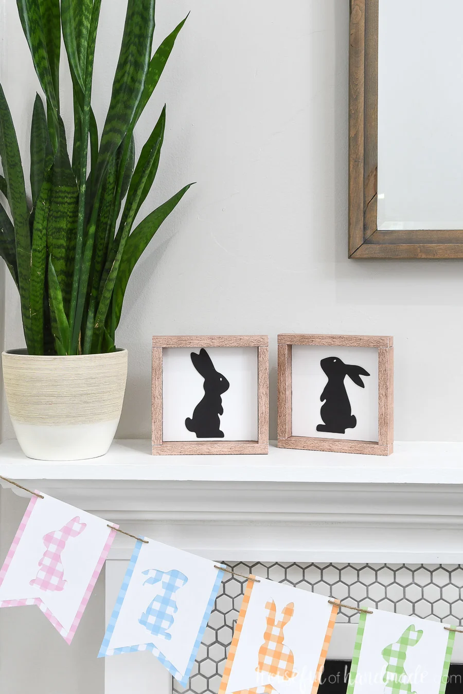 Two bunny silhouette wood signs on a mantel next to a plant.