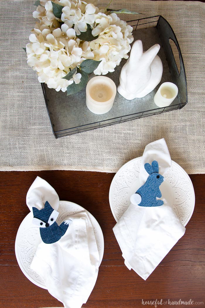 DIY bunny and fox napkin rings on a spring table sitting on white plates with white napkins inside them. 